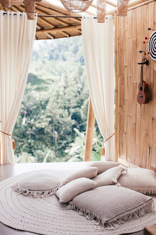 Bunch of white cushions in lounge zone decorated with drapes and ukulele on wooden wall in daylight