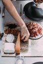 From above of unrecognizable person serving jerk meat on board with cheese at table with dishware