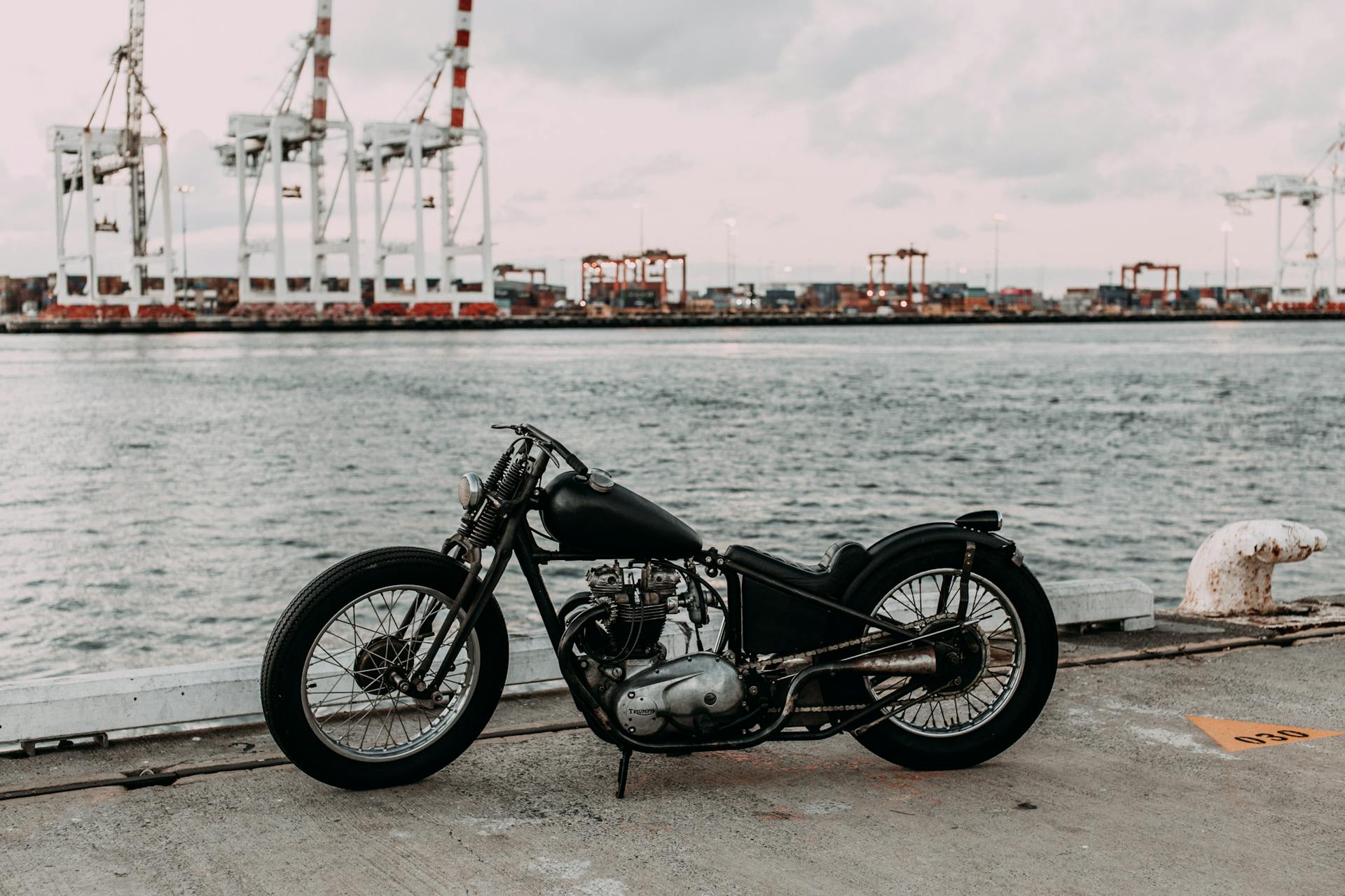 Vintage motorcycle on asphalt embankment near rippling river water against industrial area in city