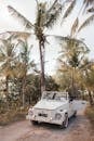 Front bumper of retro automobile on narrow roadway between greenery trees on summer day