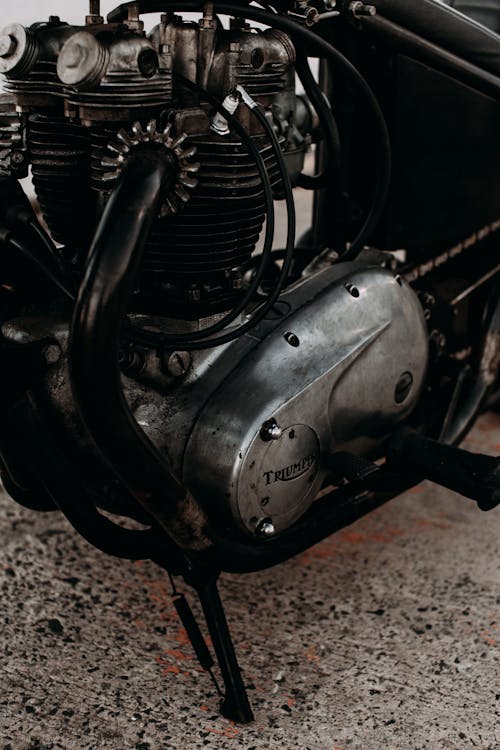 Engine under metal gear with wires of aged motorcycle parked on rough pavement in daytime