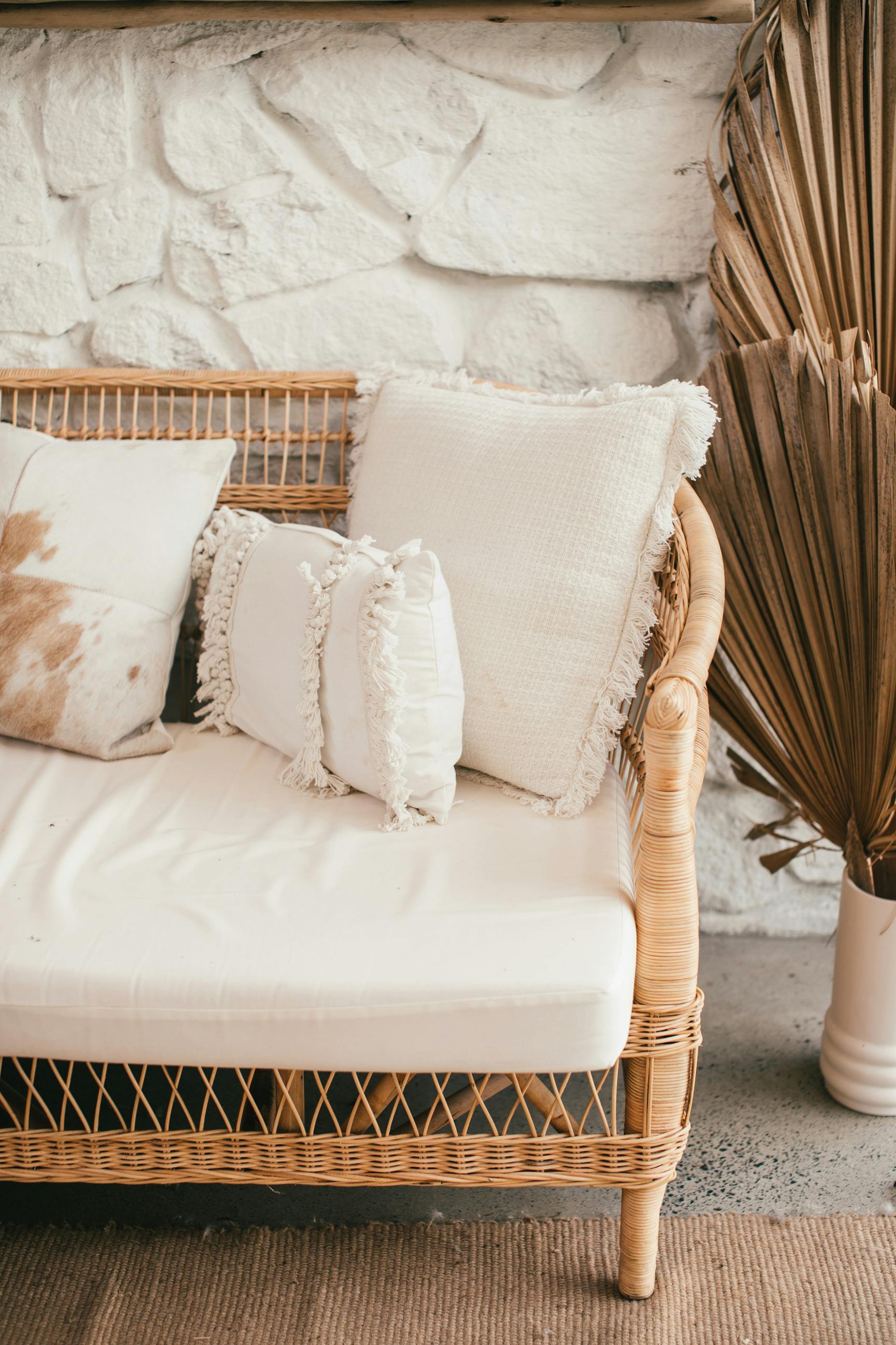 wicker sofa with decorative cushions near stone wall