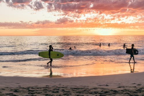 Anonymous surfers walking on sea shore at shiny sunset