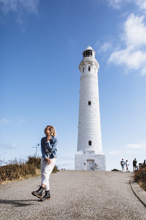 Unrecognizable traveler on road near lighthouse under cloudy sky