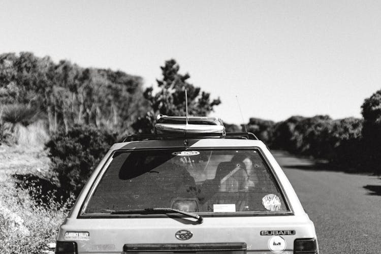 Old Car On Road Between Lush Trees In Sunlight