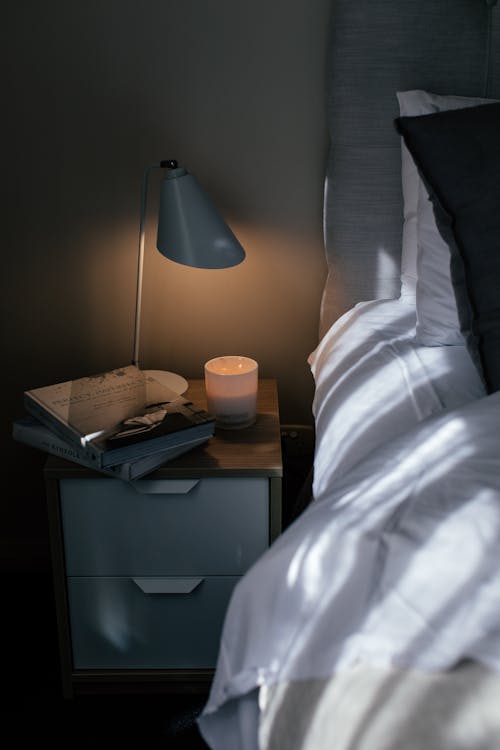Free Cozy bed with crumpled sheet and pillows near nightstand with textbooks and lamp in bedroom Stock Photo