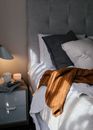 Cozy bed with pillows and knitted sweater near bedside table with mug on books in hotel room