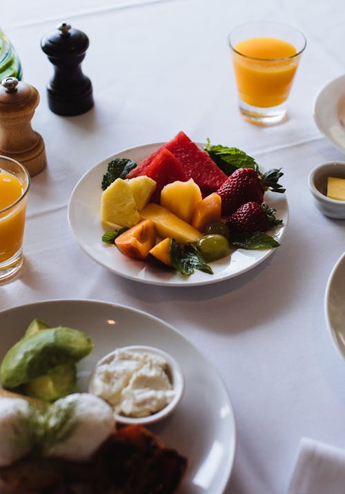 From above of appetizing assorted fruit slices near glasses of orange juice on cafeteria table