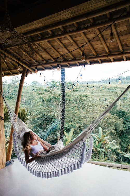 Free Young tourist lying in hammock against tropical plants on bamboo veranda while looking away in daylight Stock Photo