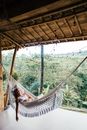 Young tired female tourist lying in hammock with fringes on bamboo veranda against exotic plants while looking at camera