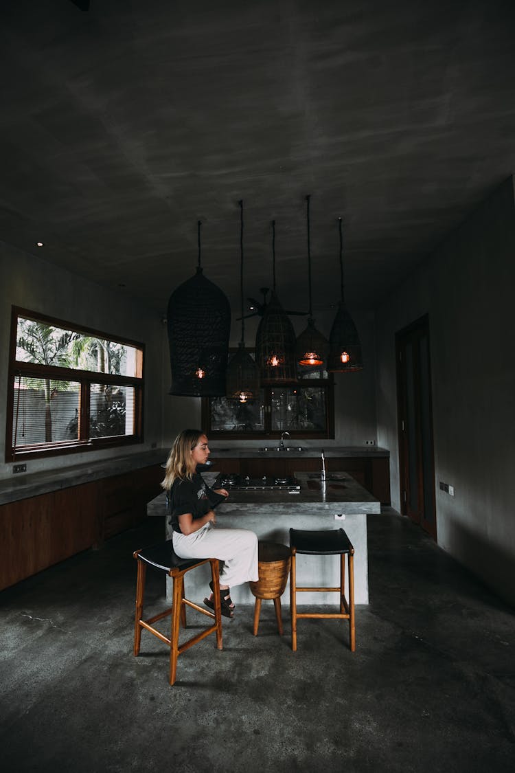 Melancholic Woman Resting On Stool In Dark Kitchen