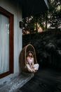 Feminine woman resting in hanging chair near house