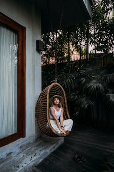 Feminine woman resting in hanging chair near house with the Quote "You don't play against opponents, you play against the game of basketball." written on it and have average color value #343634