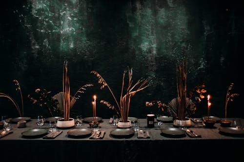 Ceramic plates with fork and knife placed on napkin on banquet table with candles and dried plants