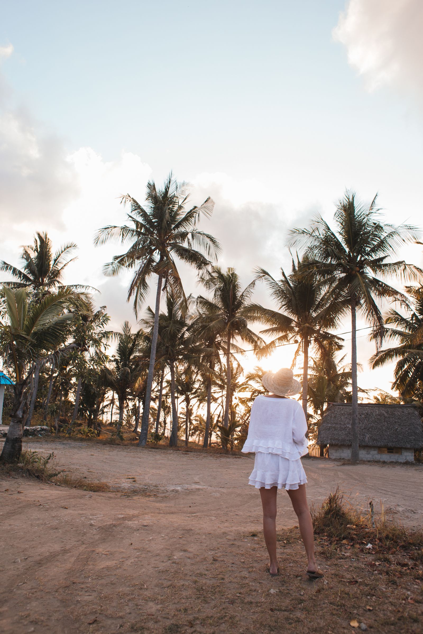 Woman in elegant white resortwear walking along a tropical beach