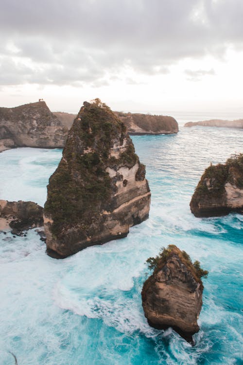 High angle of rough stony cliffs washed by blue water of sea located in tropical country under cloudy sky