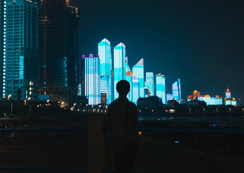 Back view of anonymous male enjoying view of high modern illuminated towers of metropolis at night