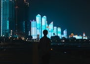 夜晚，一位匿名男子背对镜头，欣赏着大都市高耸的现代发光塔楼