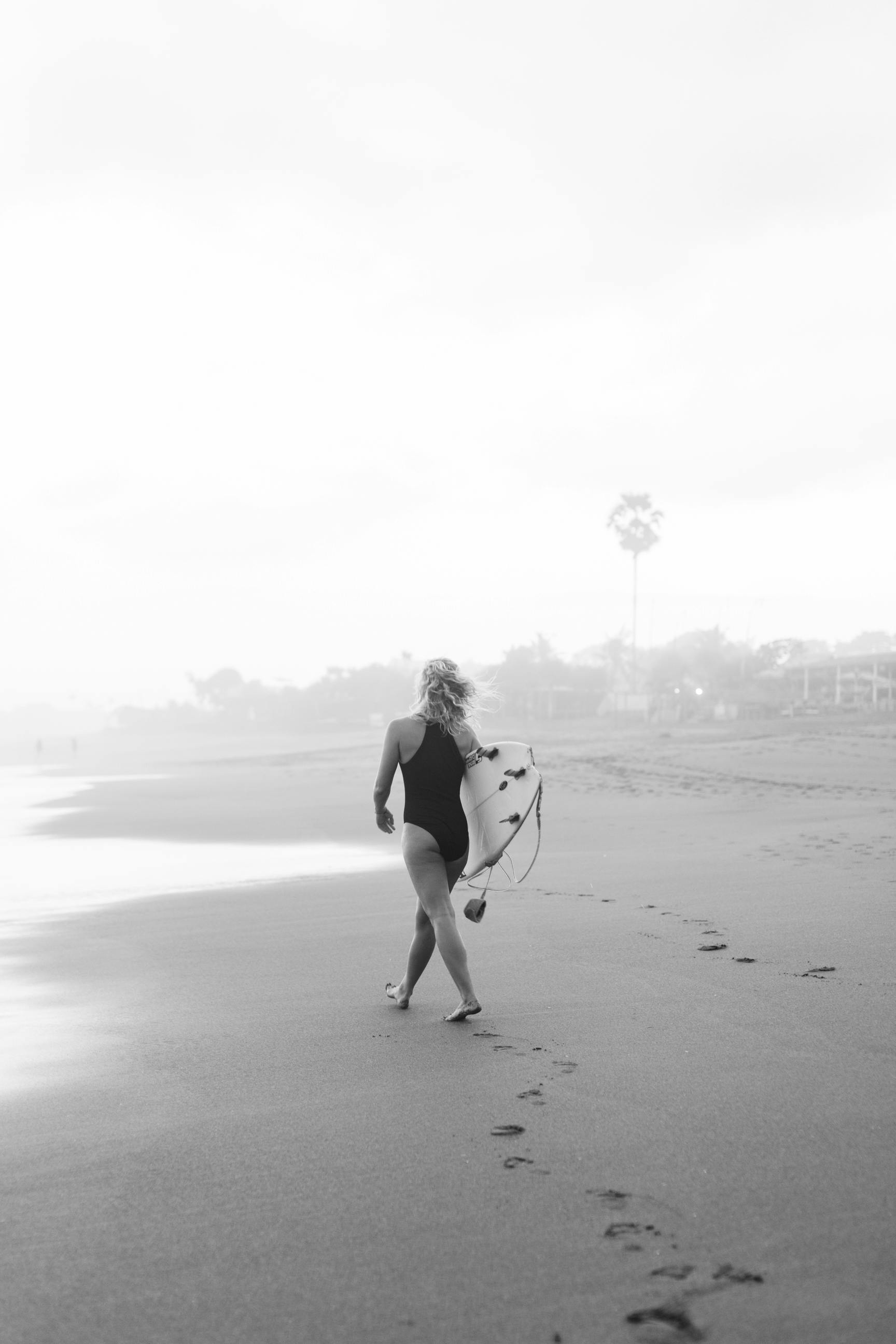 Black and white full body anonymous barefoot female surfer in swimwear walking along wet sandy coast