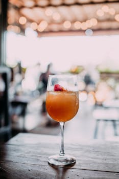 Crystal transparent goblet of fresh cold alcoholic cocktail with ice cubes placed on wooden table in cafe