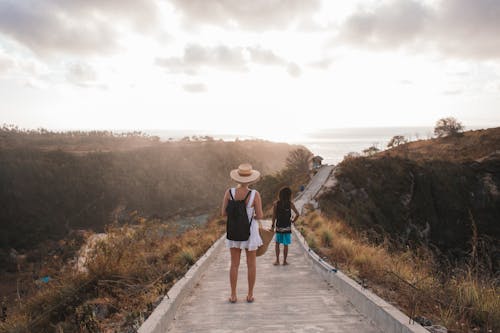 Unrecognizable mother with daughter contemplating shiny sky from walkway