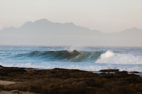 Breathtaking view of wavy sea with fast foamy water flows against rocky coast and mountain