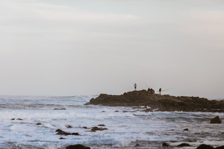 Faceless Fishermen On Rock Catching Fish In Sea