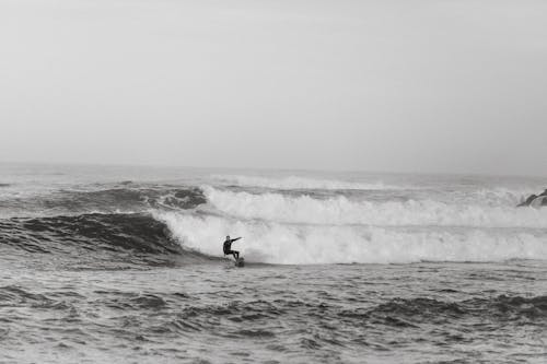Free Black and white side view of anonymous sportsman on surfboard practicing extreme sport on foamy ocean Stock Photo