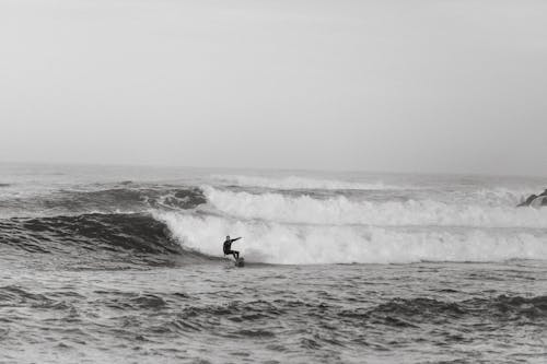 Black and white side view of anonymous sportsman on surfboard practicing extreme sport on foamy ocean