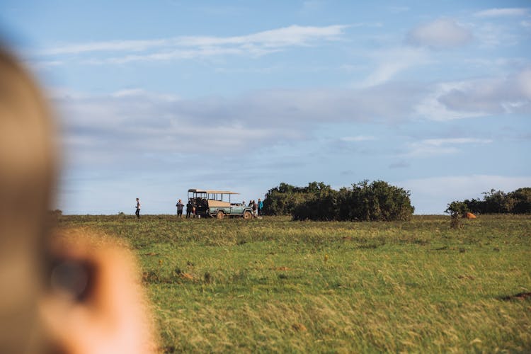 Anonymous Person Taking Photo Of Safari Car Parked In Tropical Field