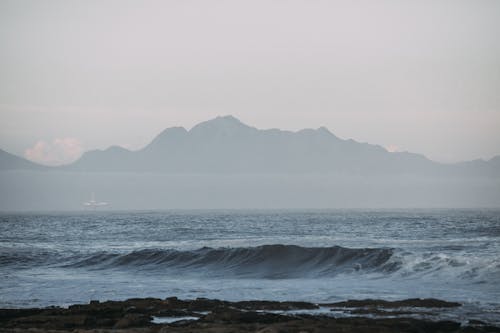 Free Coastline near waving blue sea against misty mountains Stock Photo