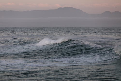 Foamy sea waves against high mountains on cloudy weather