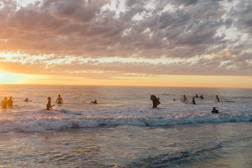 Unrecognizable tourists in swimwear admiring sea waves while swimming and splashing in water in summer evening