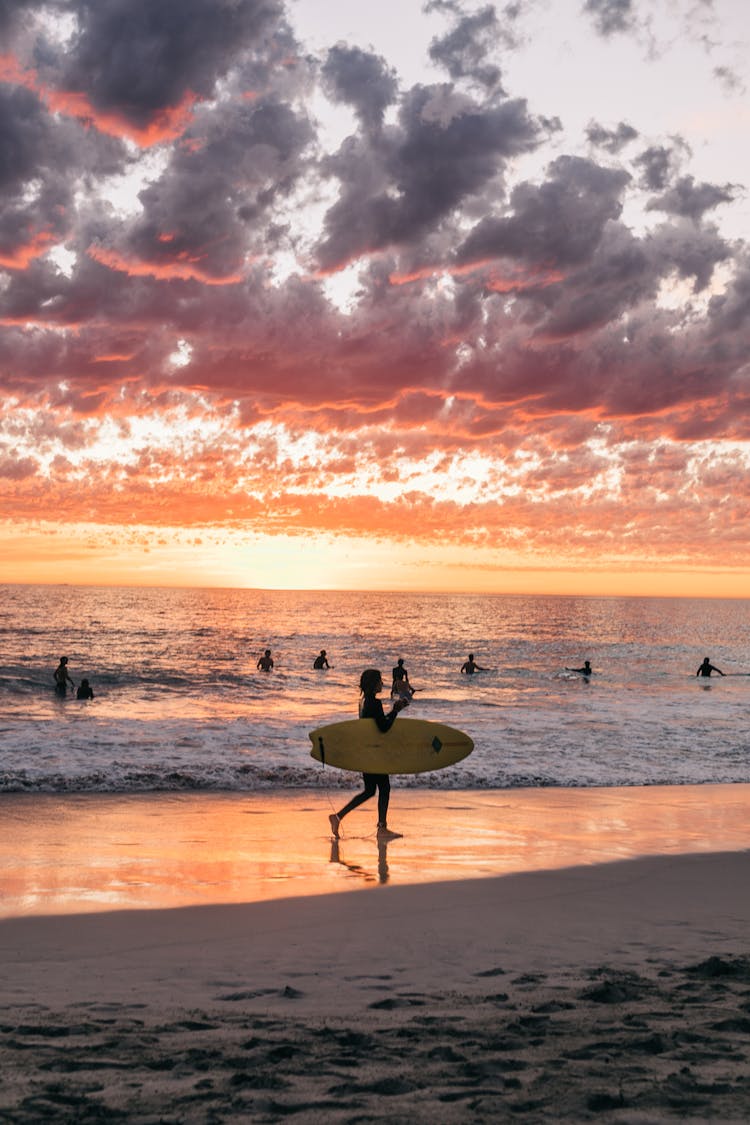 Faceless People Surfing In Ocean At Sunset