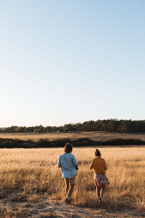 Free Back view of unrecognizable man and woman walking in dry meadow under blue cloudless sky Stock Photo