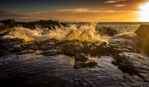 Splashing sea water near stones at colorful sunset