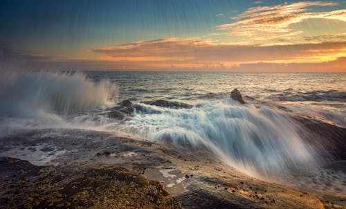 Free Rapid ocean flow with splatter on stones under bright cloudy sky at sunset in storm Stock Photo