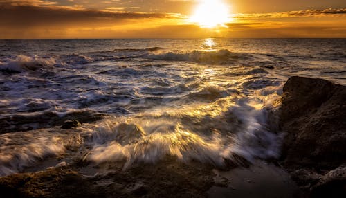 Fast sea water stream with waves and foam under colorful sky with luminous sun in twilight