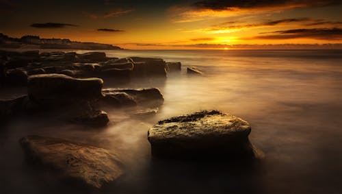 Cliffs near foggy ocean under bright sky at sunset