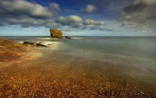 Sea water near rock under cloudy sky in fog