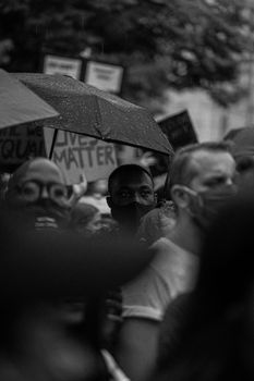 黑白图像捕捉到蒙面人群撑着伞在雨中参加抗议活动