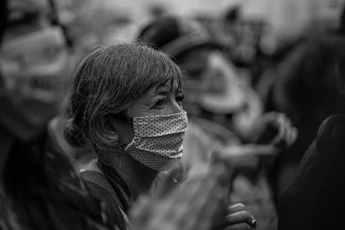 Black and white side view of unrecognizable elderly female in mask during manifestation on city street