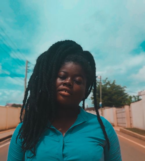 Free Mindful African American female with closed eyes and pigtails standing with tilted head on asphalt roadway under blue cloudy sky Stock Photo