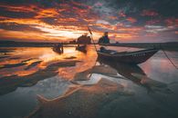 Moored fishing boats on sandy shore near bright ocean and anonymous friends under bright cloudy sky at sunset
