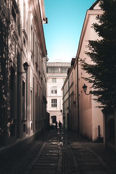 Uneven walkway with silhouettes of unrecognizable couple between aged stone house exteriors in town