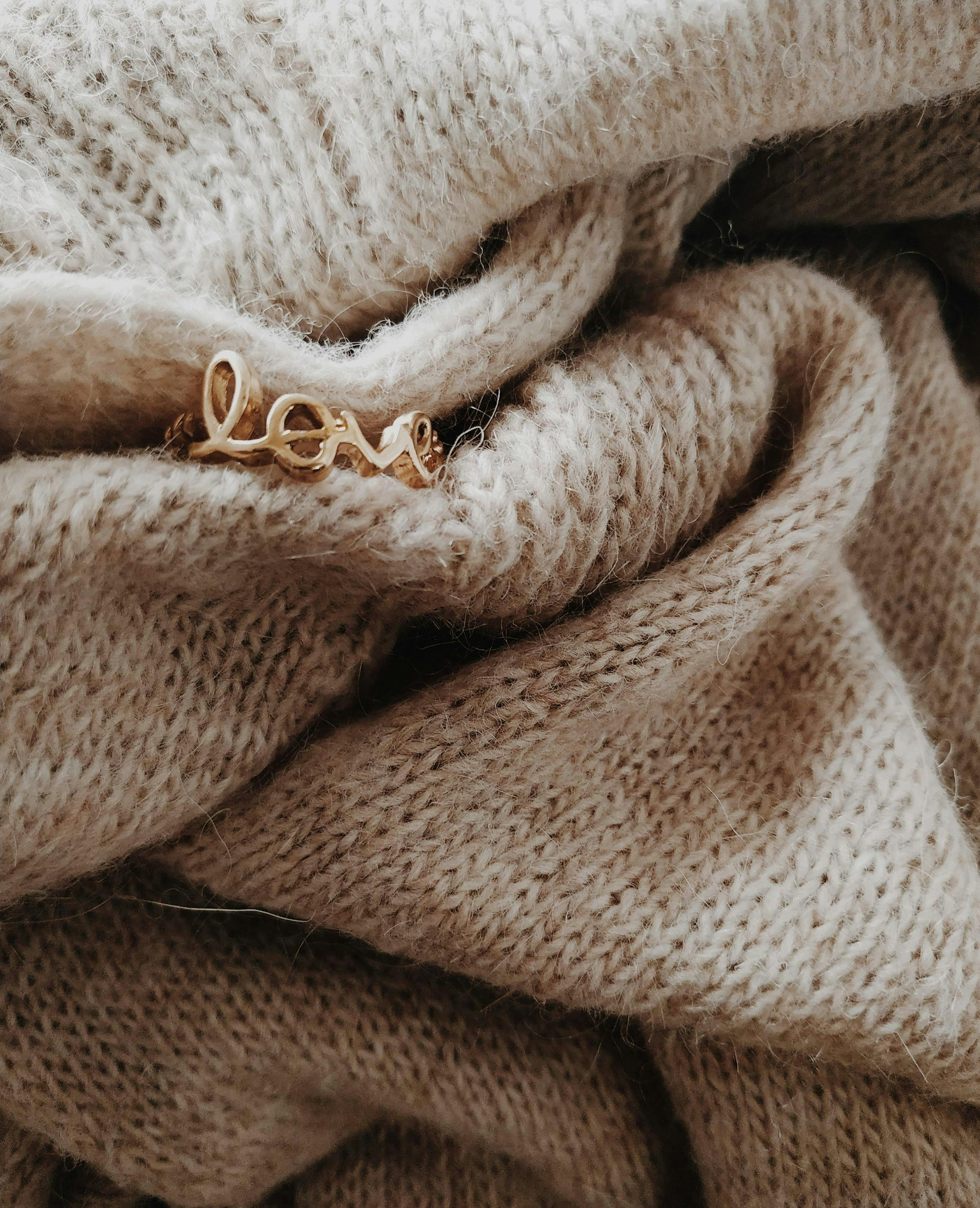 Close-up of a beige wool sweater adorned with love-themed jewelry, highlighting texture and warmth.