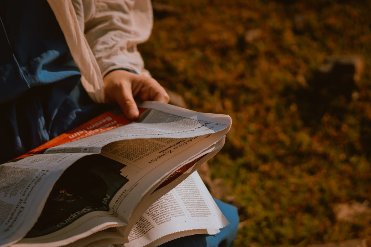 Person reading a newspaper outdoors on a green meadow, seen from above.