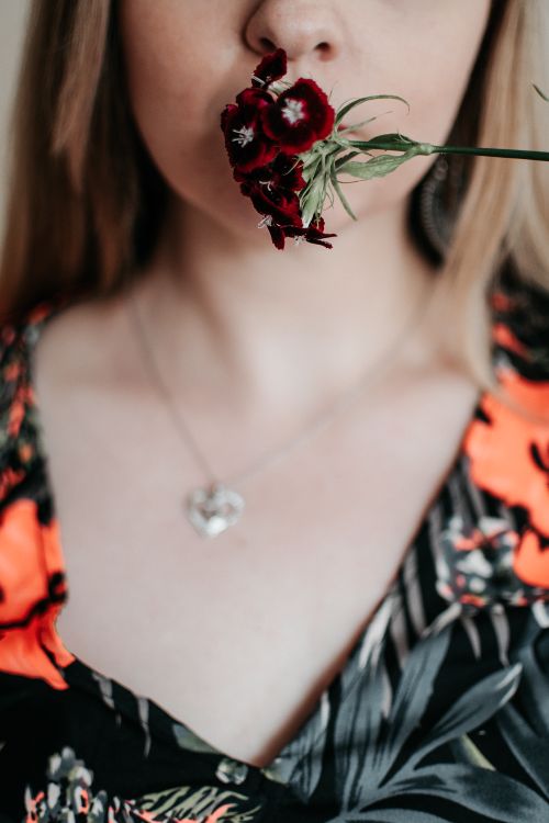 Free Crop anonymous female in pendant and ornamental wear covering lips with blossoming flower on thin stalk Stock Photo