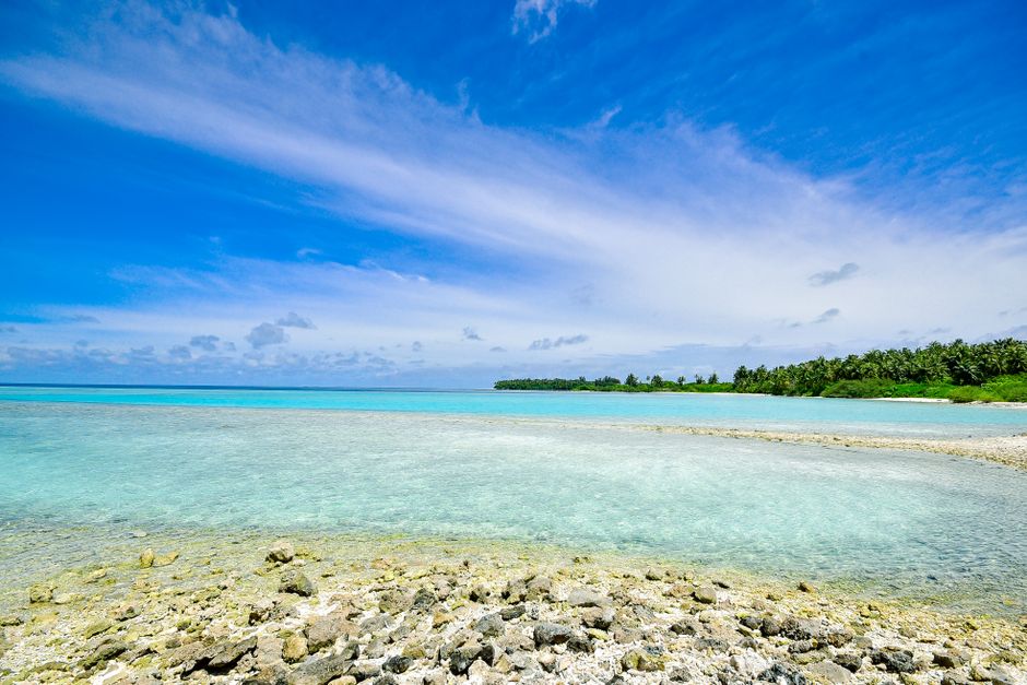 A peaceful tropical seascape featuring clear blue waters, white clouds, and lush greenery in Laamu Atoll, Maldives.