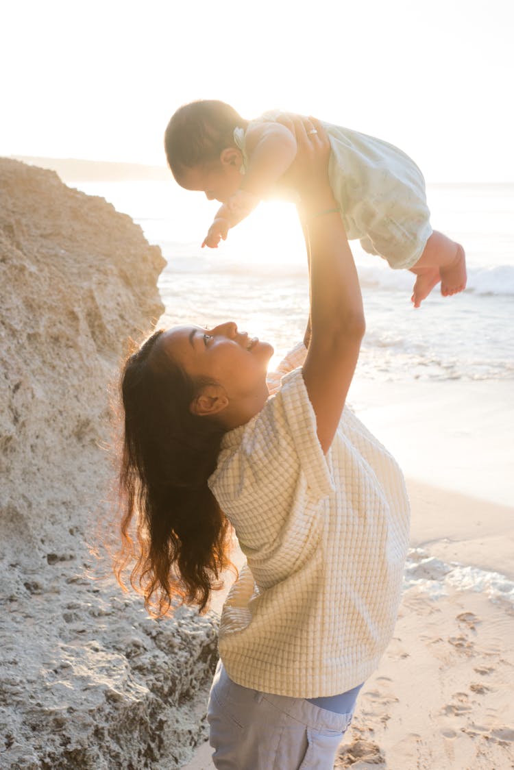 Woman Raising Baby Up On Beach